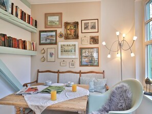 A cozy room with a wooden table, a chair, a bookshelf, and framed pictures on the wall.