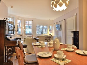 A dining area with a piano, chairs, a table set for two, and a large window with a view.
