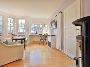 A modern living room with a sofa, a dining table, and a kitchen area with a refrigerator and a microwave.