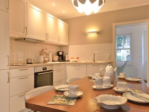 A modern kitchen with white cabinets, a dining table set for tea, and a view of the outside through a window.