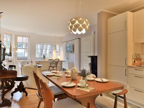 A dining area with a wooden table, chairs, a hanging light fixture, and a view of the kitchen.