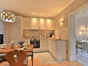 A modern kitchen with white cabinets, a dining table, and a hanging light fixture.