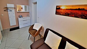 Une chambre d’hôtel avec un lit, une chaise, une commode, un miroir et un tableau accroché au mur représentant un coucher de soleil sur un champ.