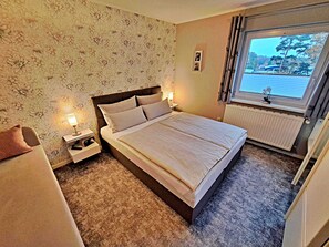 Una camera da letto con un letto, comodini, una finestra con vista e un termosifone.