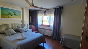 A bedroom with a bed, a nightstand, a chair, a window with curtains, a radiator, and a ceiling fan. - Margasol - Housing for Tourist Use (PEDREZUELA)