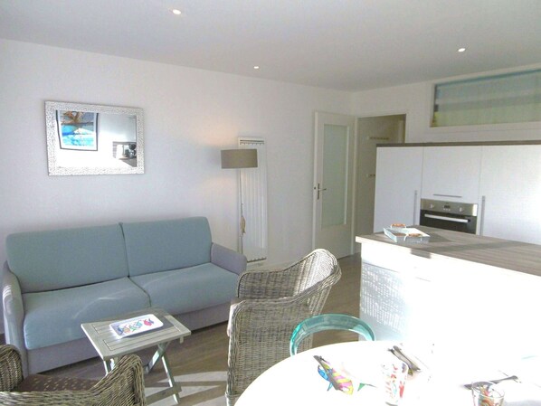 A compact living space with a sofa, wicker chairs, a small table, a kitchen area with an oven, and a mirror on the wall. - Studio cabin 2 to 4 people Ocean view (SARZEAU)
