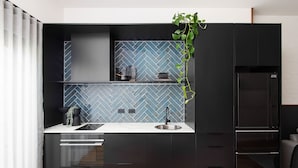 Une cuisine moderne avec des meubles de couleur noire, un dosseret de carrelage en motif chevron, un évier en acier inoxydable et un four encastré.