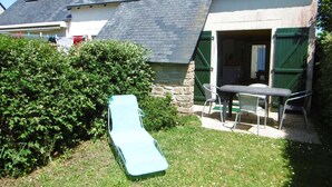 Una casa con techo inclinado, pared de piedra y un pequeño patio con mesa y sillas.