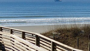 A wooden boardwalk leading to a beach with a ship in the distance.