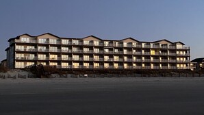 A multi-story hotel with balconies, located near a beach.