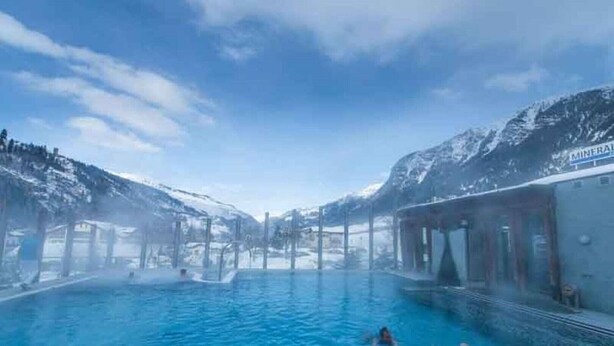 A pool area with a clear view of the mountains in the background, a covered seating area, and a sign that reads "MINERAL SPA".
