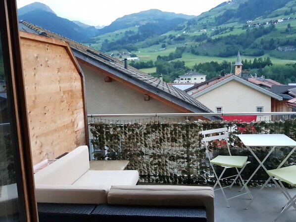 A balcony with a wooden slat wall, a sofa, and two chairs.