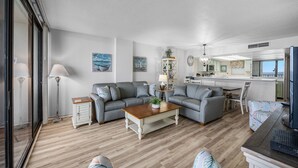 Ein modernes Wohnzimmer mit grauem Sofa, einem Holztisch und einem Essbereich mit weißem Tisch und Stühlen.