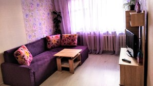 A living room with a purple sofa, a wooden coffee table, a TV on a wooden stand, and a window with sheer curtains. - Fontanskaya doroga 16/5 (Одесса)