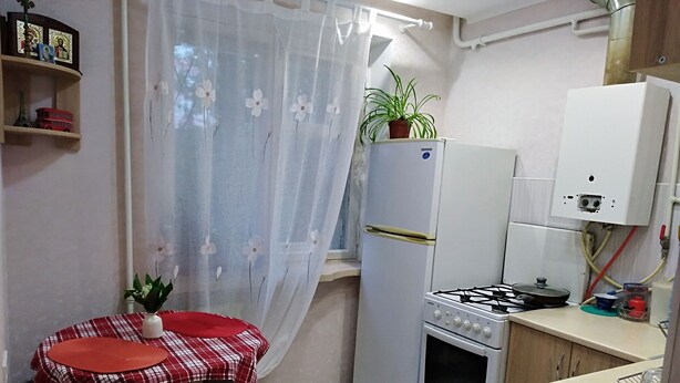 A compact kitchen with a gas stove, a refrigerator, and a dining table with a red and white checkered tablecloth. - Fontanskaya doroga 16/5 (Одесса)