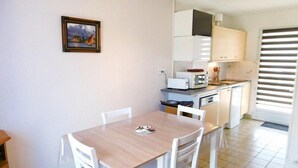 Cocina compacta con armarios blancos, microondas y tostadora. Hay una mesa de comedor con sillas y un cuadro en la pared.