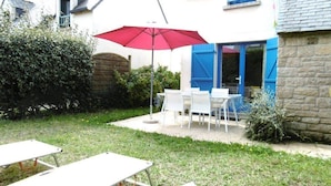 Un patio con mesa y sillas, un paraguas rojo y una pared de piedra.