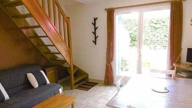 Una sala de estar con sofá, una mesa de madera, una escalera y un vidrio corredero que da a un balcón.