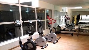 Ett gym med olika typer av träningsutrustning, stora fönster och en person i bakgrunden.