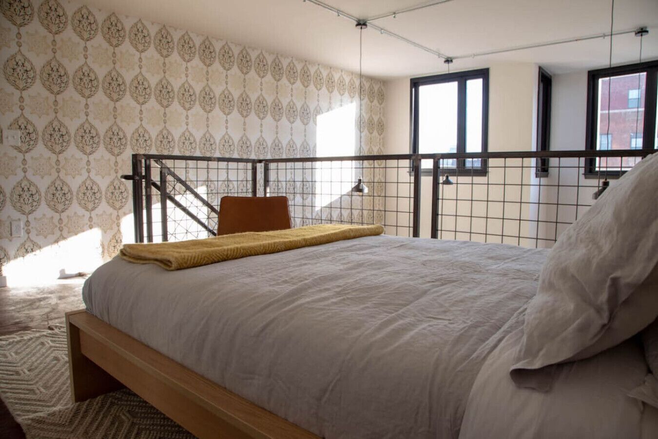 Een slaapkamer met een bed, een houten bankje, een stoel, een raam en behang met een patroon.