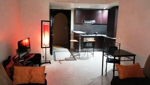 Ett vardagsrum med en soffa, en tv och en lampa. Det finns också ett köksområde med skåp och ett matbord.