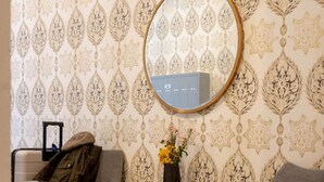 A room with two grey armchairs, a small wooden side table with a vase of flowers, and a wall-mounted mirror reflecting a thermostat. - Poor Richard Studio at The Kestrel (Philadelphia)