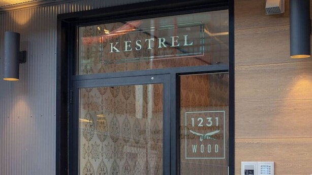 A hotel entrance with a glass door, a wooden wall, and a fire hydrant outside. - Poor Richard Studio at The Kestrel (Philadelphia)