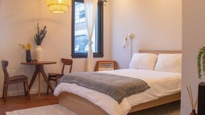 A neatly arranged bedroom with a bed, bedside table, chair, and a small table with a lamp.