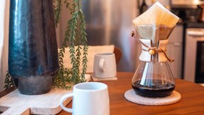 A coffee maker on a wooden table with a white mug and a white cup.