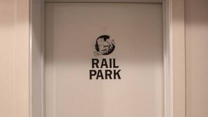 A white door with a "RAIL PARK" sign and a doormat with a "K" symbol.