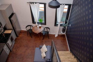 A compact kitchen with modern appliances, a dining area with a round table and two chairs, and a staircase leading to another level. - Hive Room Loft at The Kestrel (Philadelphia)