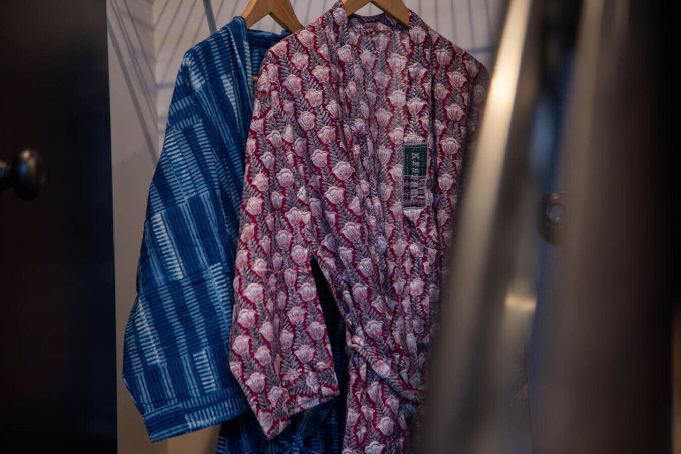 A closet with two patterned garments hanging on a wooden hanger.