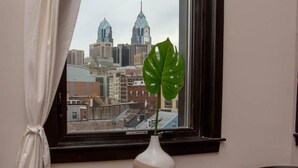 A room with a view of a city skyline through a window with a curtain. - Hive Room Loft at The Kestrel (Philadelphia)