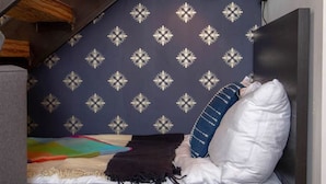 A compact, modern bedroom with a sloped ceiling, a bed with white and blue bedding, a colorful rug, and a decorative wall with a snowflake pattern. - Hive Room Loft at The Kestrel (Philadelphia)