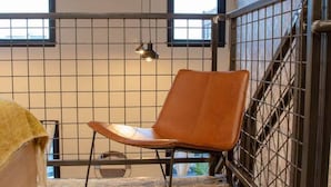 A room with a patterned rug, a brown leather chair, a bed with a yellow blanket, a window, and a metal gate. - Reading Viaduct Loft at The Kestrel (Philadelphia)