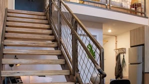A staircase with wooden steps and metal railings leading to a lofted area with a bed and a chair. - Reading Viaduct Loft at The Kestrel (Philadelphia)