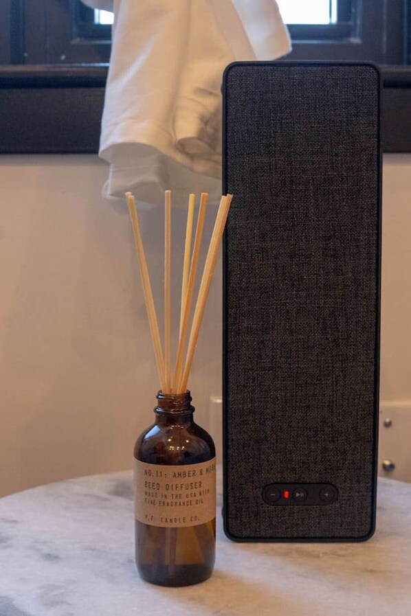 Un diffuseur de parfum à bâtonnets aux notes d’ambre et de musc, placé à côté d’un smartphone sur une surface en marbre.