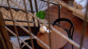 A round wooden table with a white vase and a green plant, a black chair, and a metal railing in the foreground. - Mayor`s Study Loft at The Kestrel (Philadelphia)