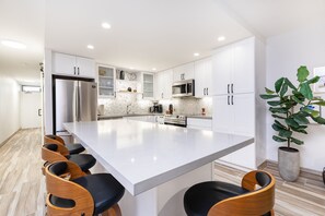 Une cuisine moderne avec des meubles blancs, un grand îlot central et des tabourets de bar.