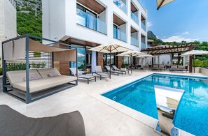 A modern outdoor pool area with lounge chairs, umbrellas, and a pergola.