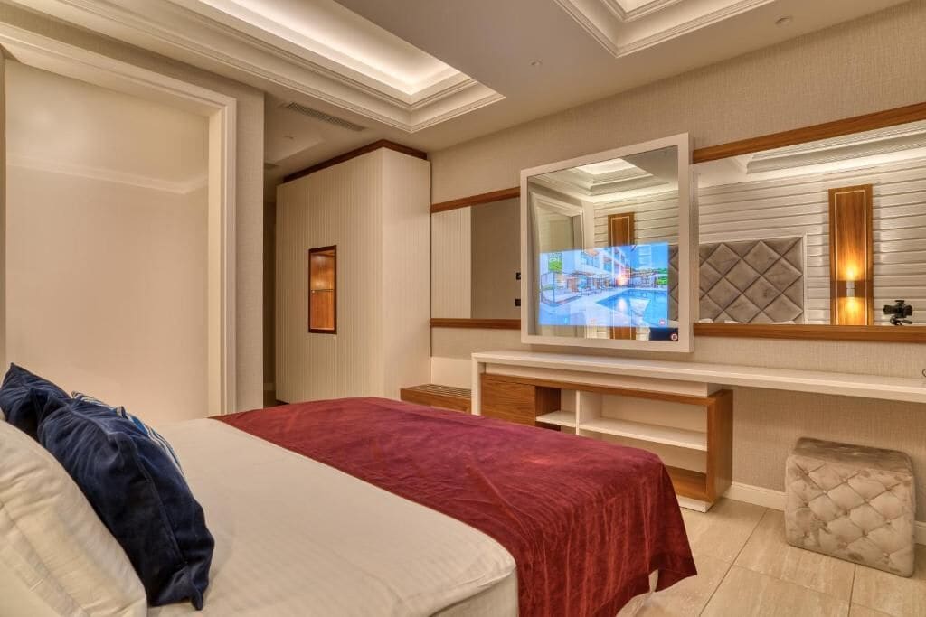 A hotel room with a bed, a TV, a mirror, and a small seating area.