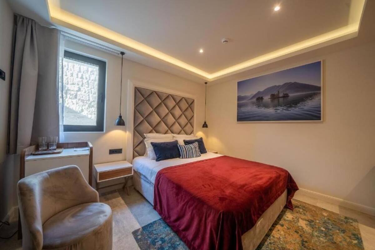 Quarto de hotel com cama, escrivaninha, cadeira, janela com cortinas, quadro pendurado na parede e luminária no teto.