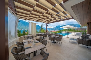 An outdoor patio with tables and chairs, a pool, and mountains in the background.