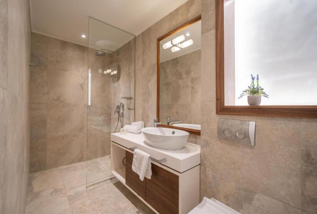 Un baño moderno con un espejo grande, un lavamanos pedestal, ducha y una planta en maceta.