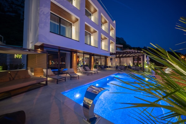 A modern hotel with a swimming pool, outdoor seating, and a well-lit facade.
