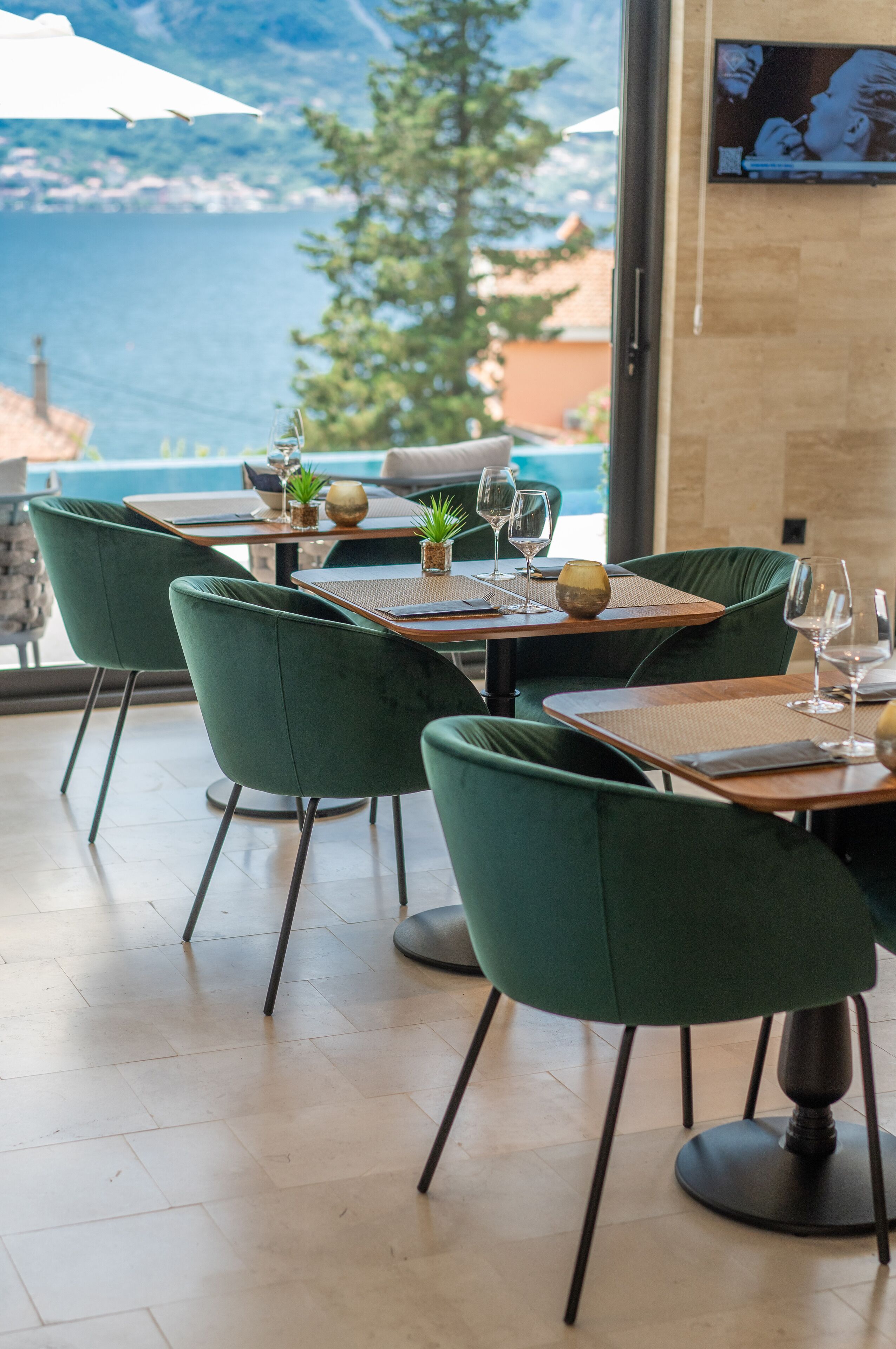 Un restaurante con sillas de terciopelo verde, mesas de madera y vista al mar.