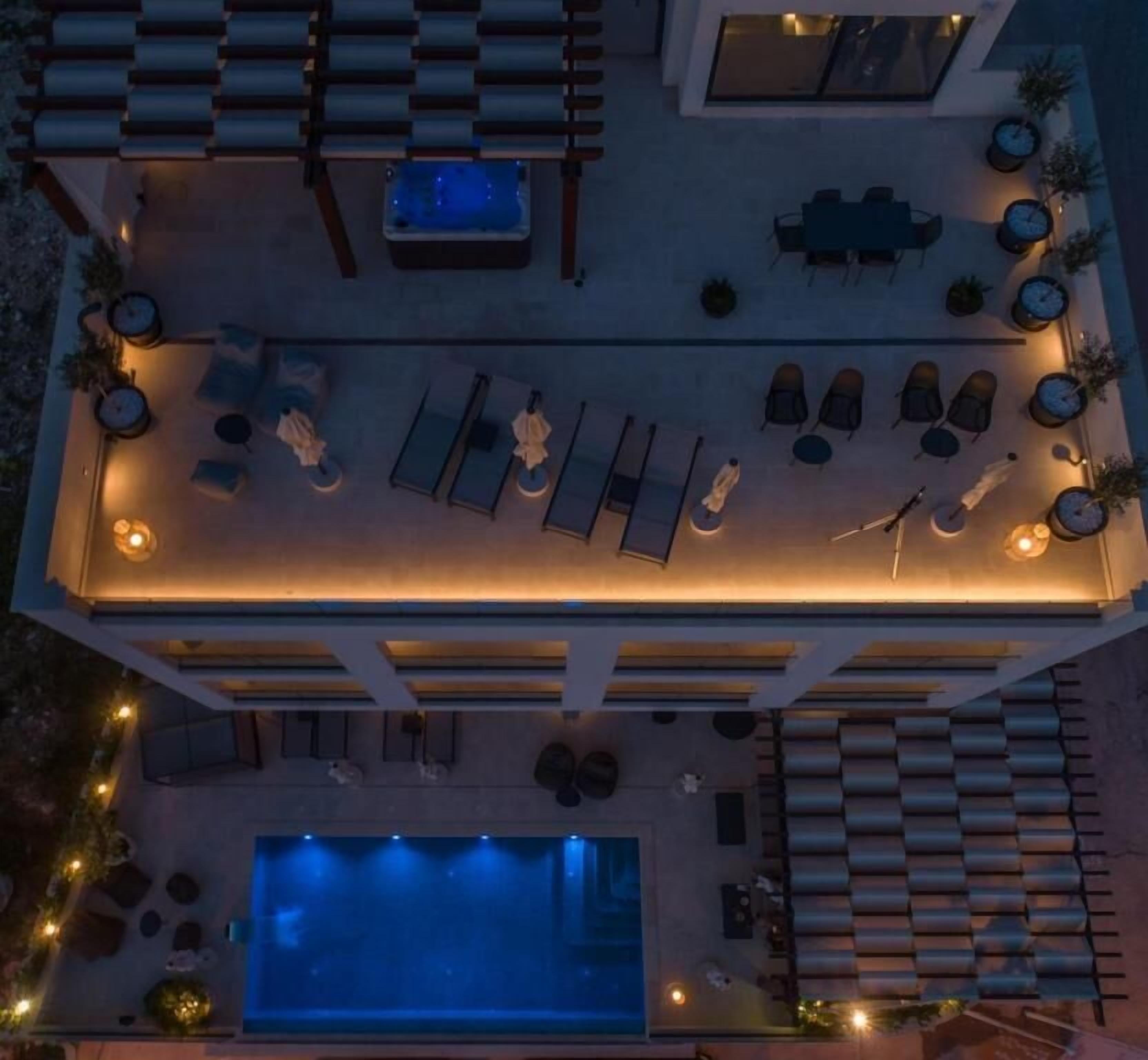 Vista aérea de un moderno área de piscina al aire libre con sillones de descanso, una bañera de hidromasaje y una piscina.