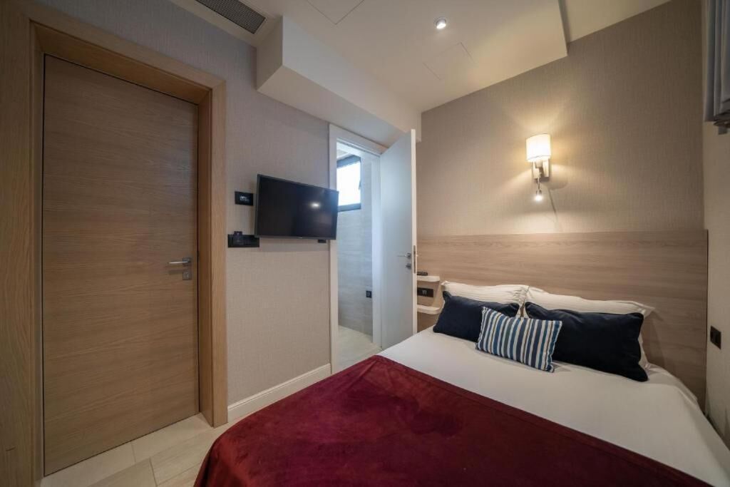Una habitación de hotel con una cama, un televisor, una lámpara de pared y una puerta.