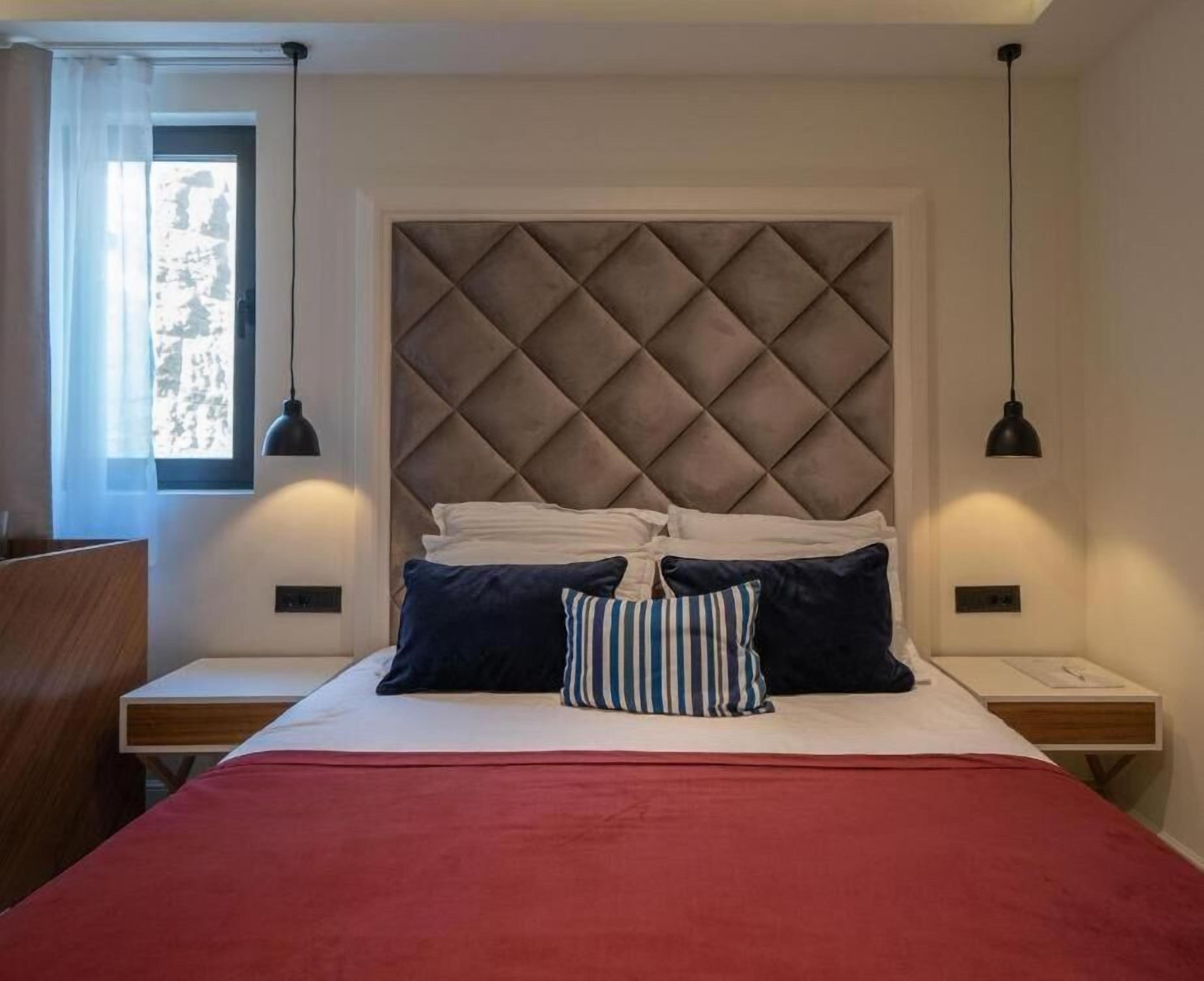 Ein Hotelzimmer mit Bett, Kopfteil, Nachttischen und einem Fenster.