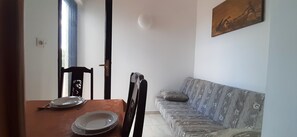 A dining area with a table set for two, a sofa, and a painting on the wall.